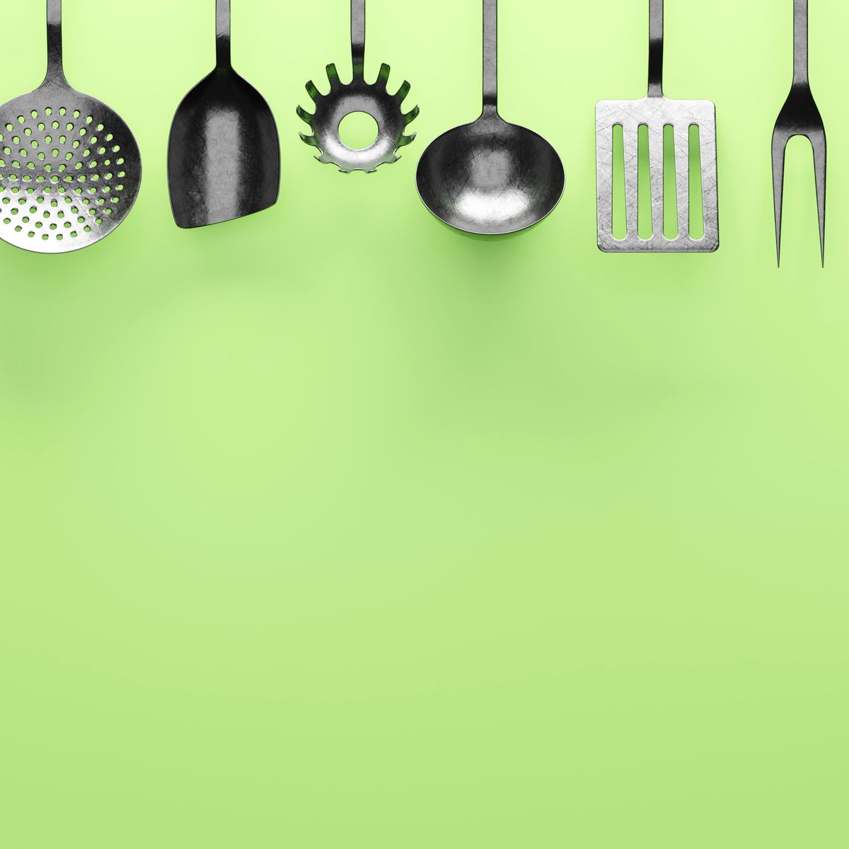 Steel kitchen utensils hanging on a green wall