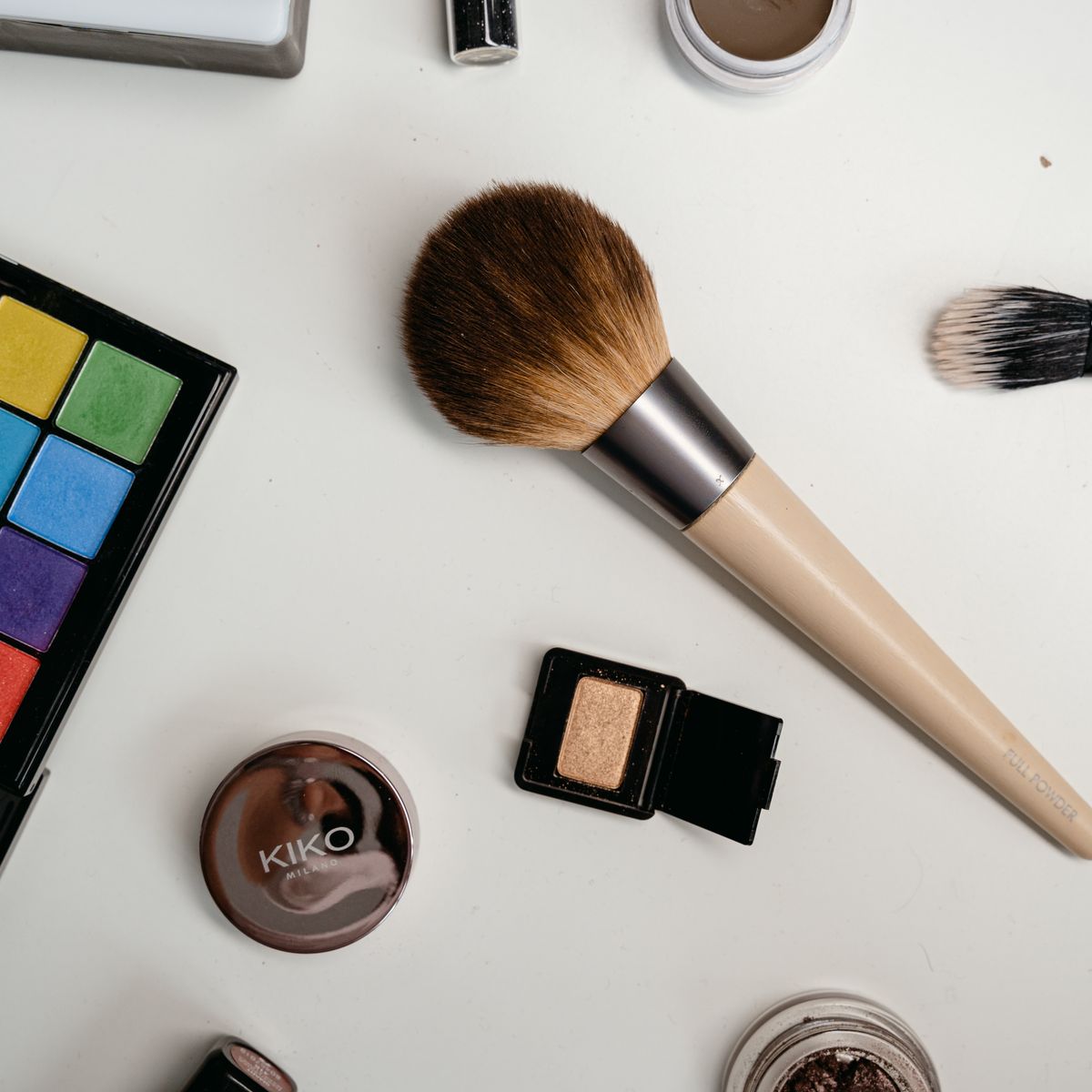 Makeup brush, eyeshadow palette and powders on a white table
