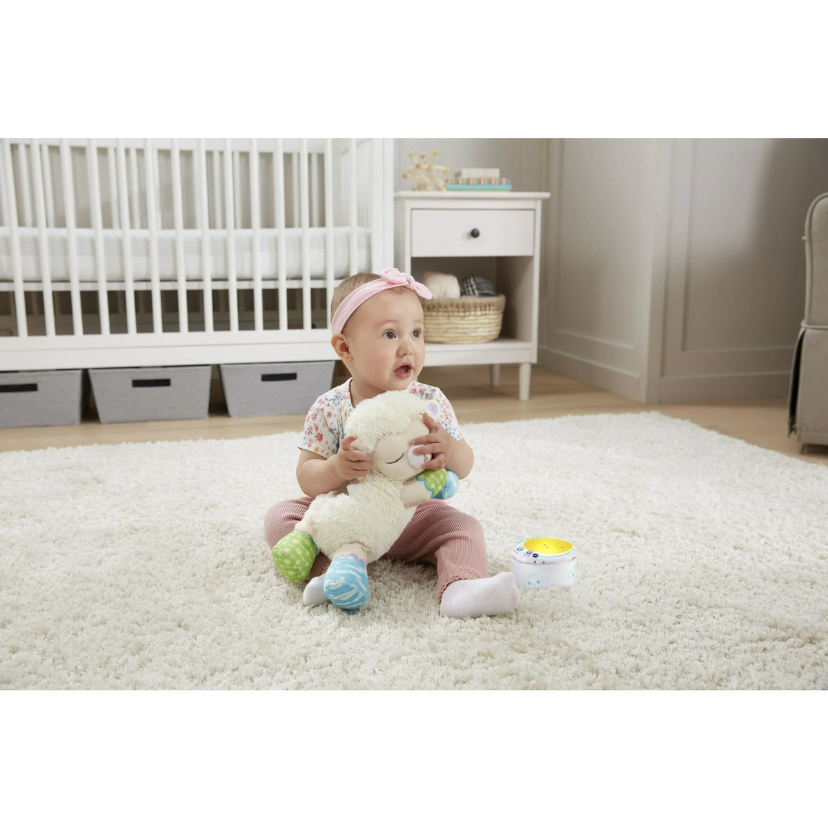 Baby in a pink headband hugging the plush lamb on a nursery rug