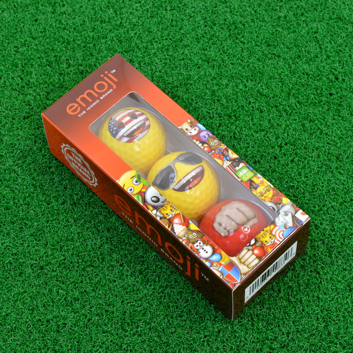 Emoji golf ball 3-pack in its window box lying on green turf
