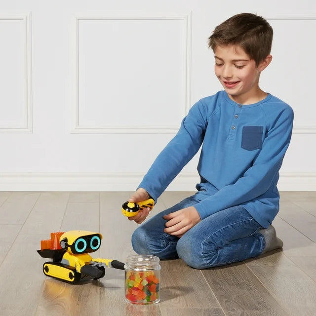 Smiling boy driving the yellow robot with a hand remote to grab a jar of sweets