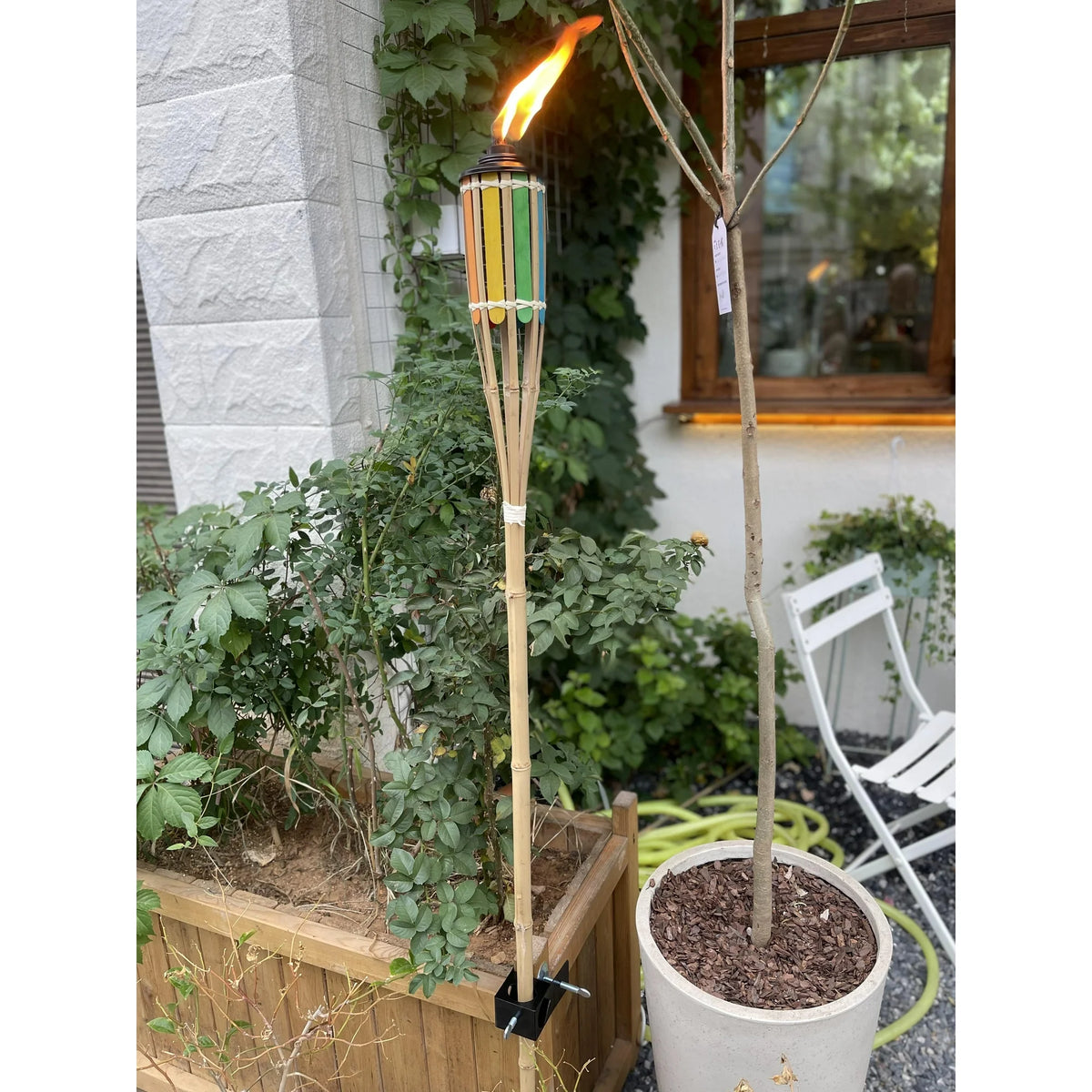 Lit rainbow bamboo garden torch held upright by a black clamp on a wooden planter