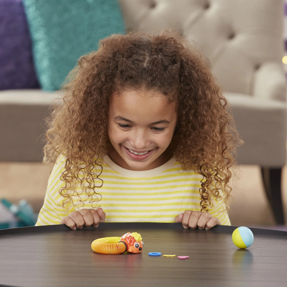 Excited girl peering over a table edge at the clownfish spring toy and its ball