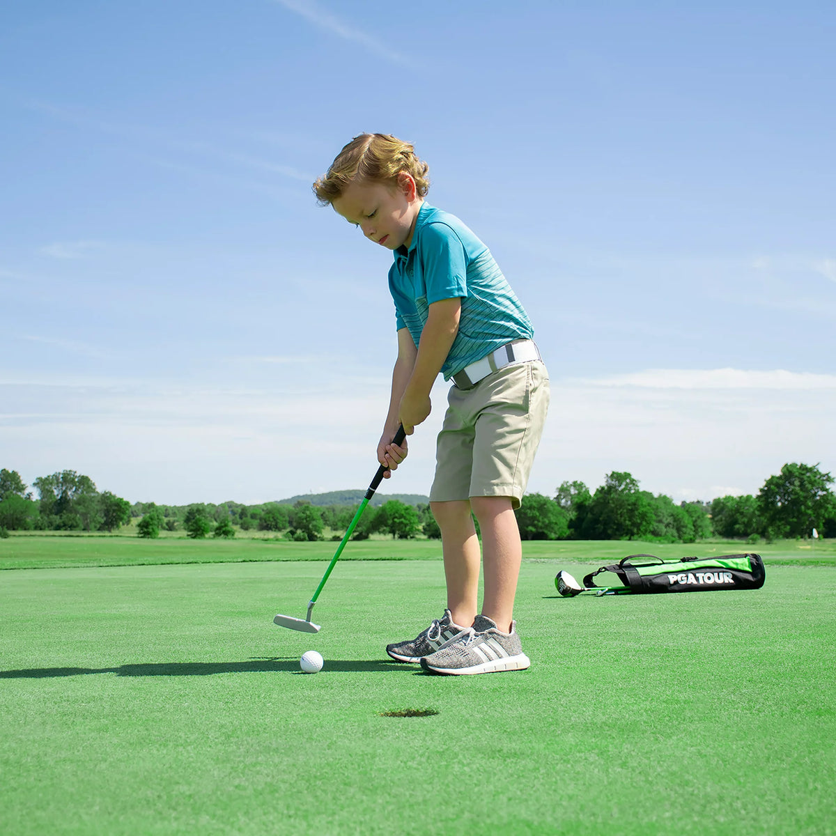 Young boy putting on a green with the junior bag and driver lying behind