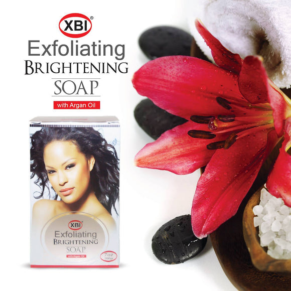 Box of exfoliating brightening soap with argan oil beside a red lily, spa stones and bath salts