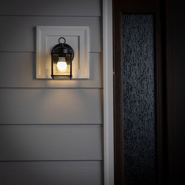Lit lantern wall light on a white mounting block beside a dark front door