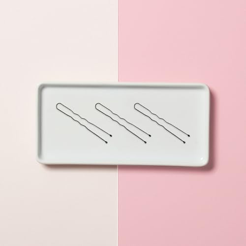 Three black wavy hair pins on a white tray against pink