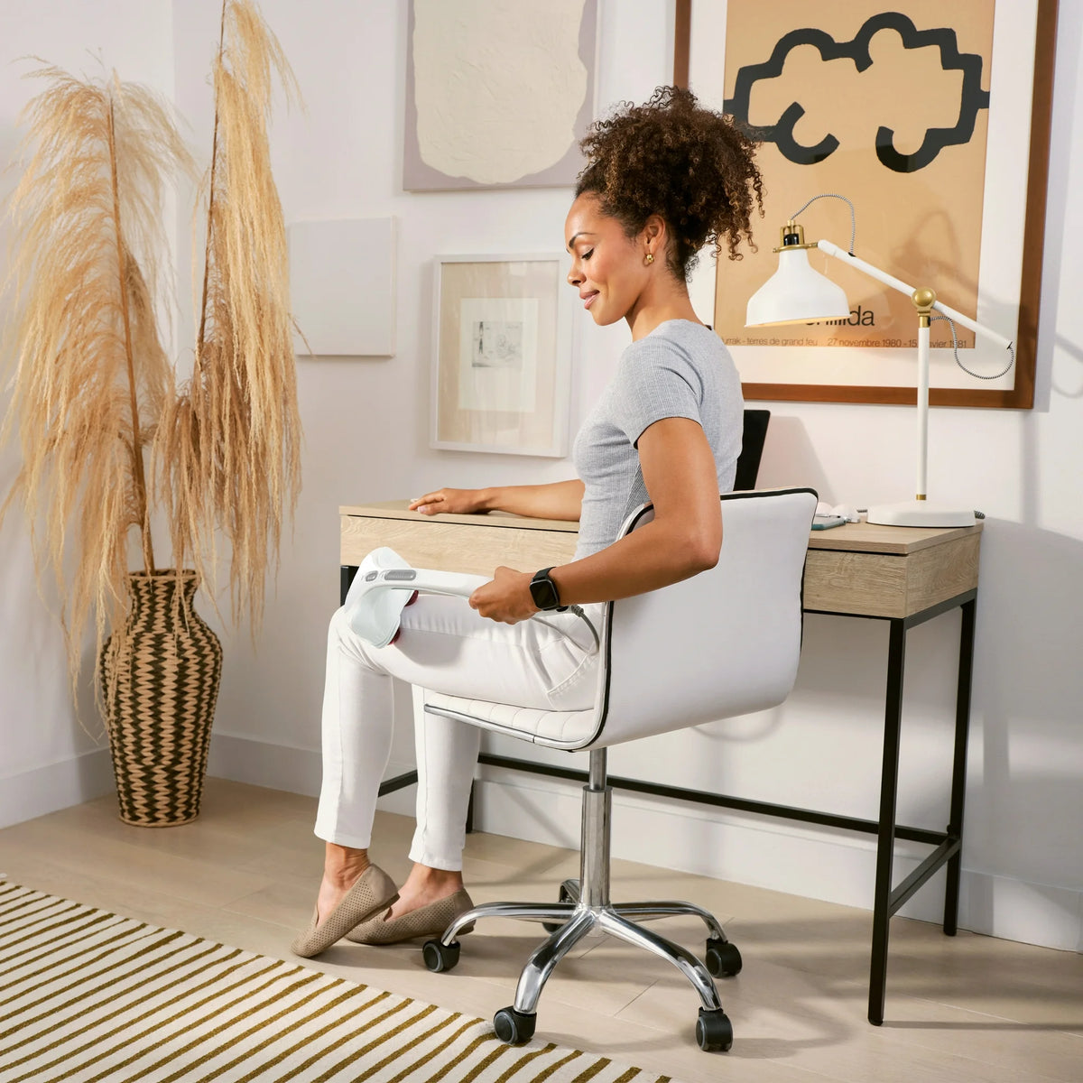 Woman in an office chair using the white massager on her thigh
