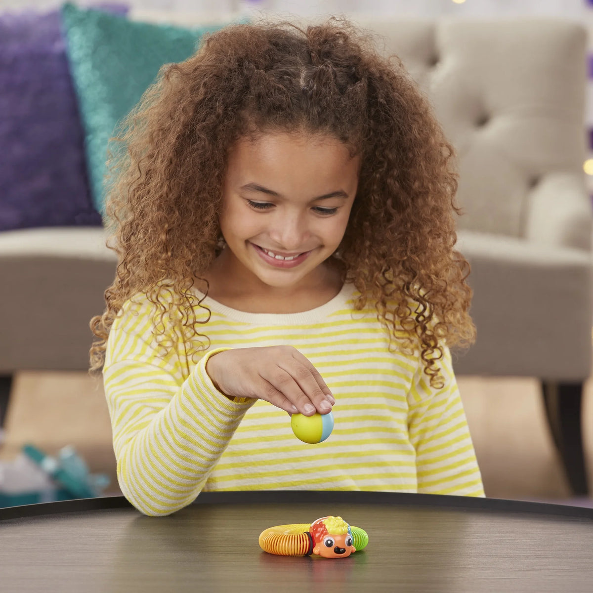 Girl in a striped top holding the ball above the clownfish spring toy on a table