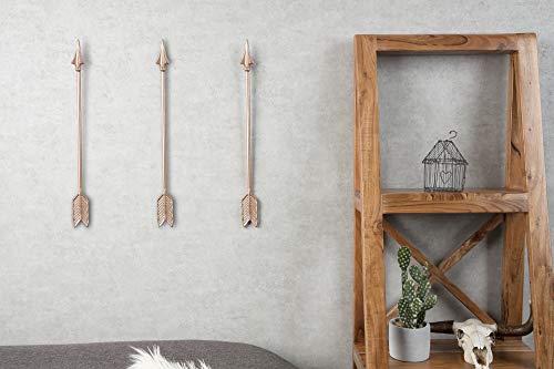 Three copper-painted arrows hung on a grey wall beside a wooden shelf