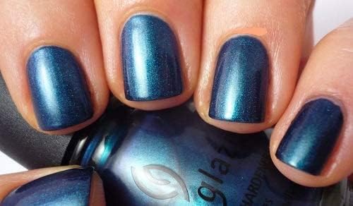 Fingernails painted deep blue shimmer polish beside the matching bottle