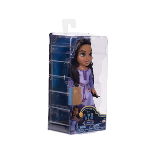 Small angled view of the boxed doll in a lilac tunic holding a tan book