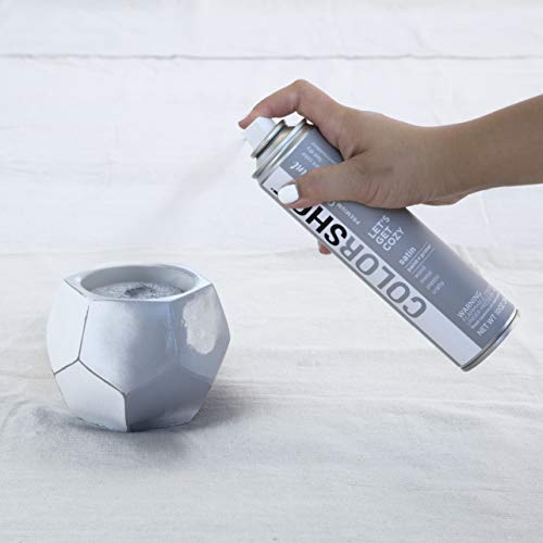 Hand spraying grey paint onto a white geometric planter