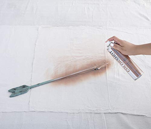Hand spraying copper paint along a teal metal arrow on a drop cloth