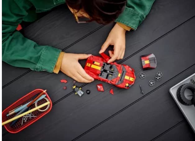 Child building the red brick car on a dark wood table with loose wheels and parts