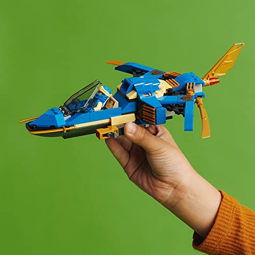 Child's hand flying the blue and gold brick jet against a green background