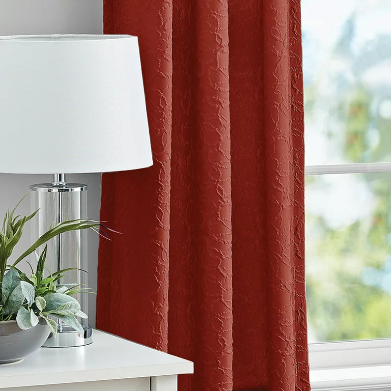 Rust red textured curtain beside a white table lamp and plant