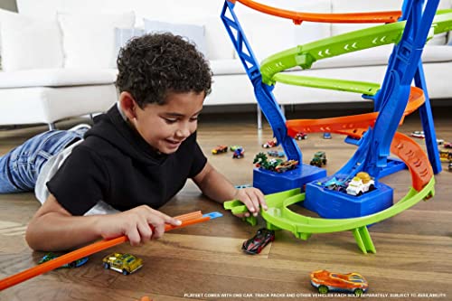 Boy on the floor launching a car into the spiral track surrounded by toy cars
