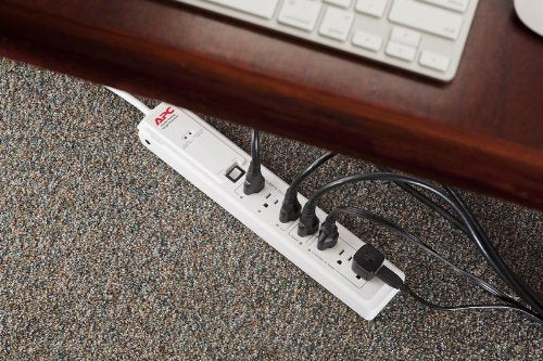 White surge protector on a carpet under a desk with several black plugs connected