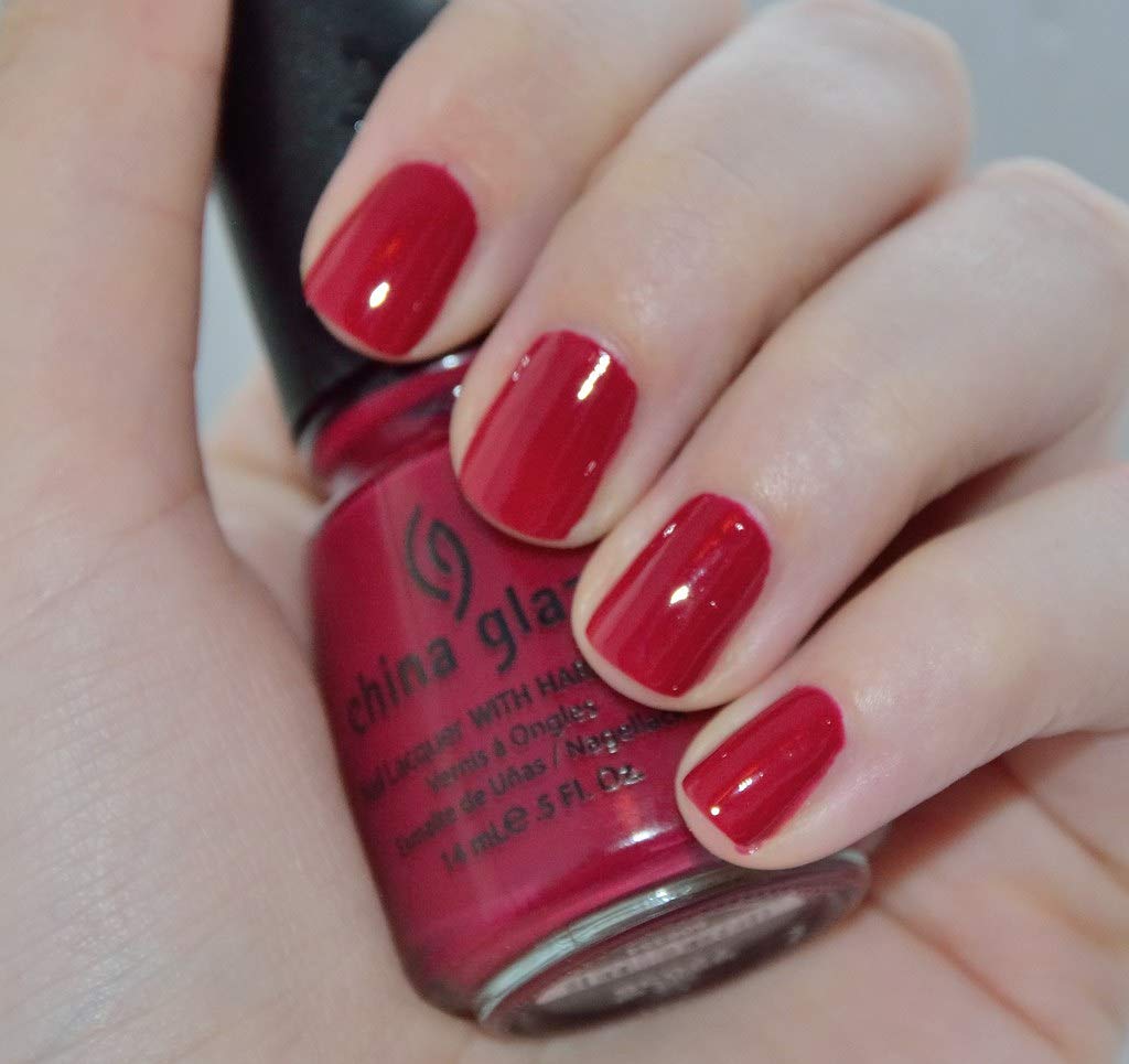 Close-up of nails in glossy raspberry red holding the bottle