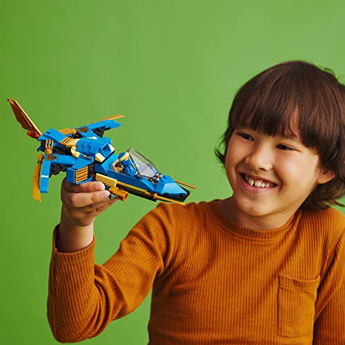 Smiling child in an orange sweater holding up the brick-built ninja jet