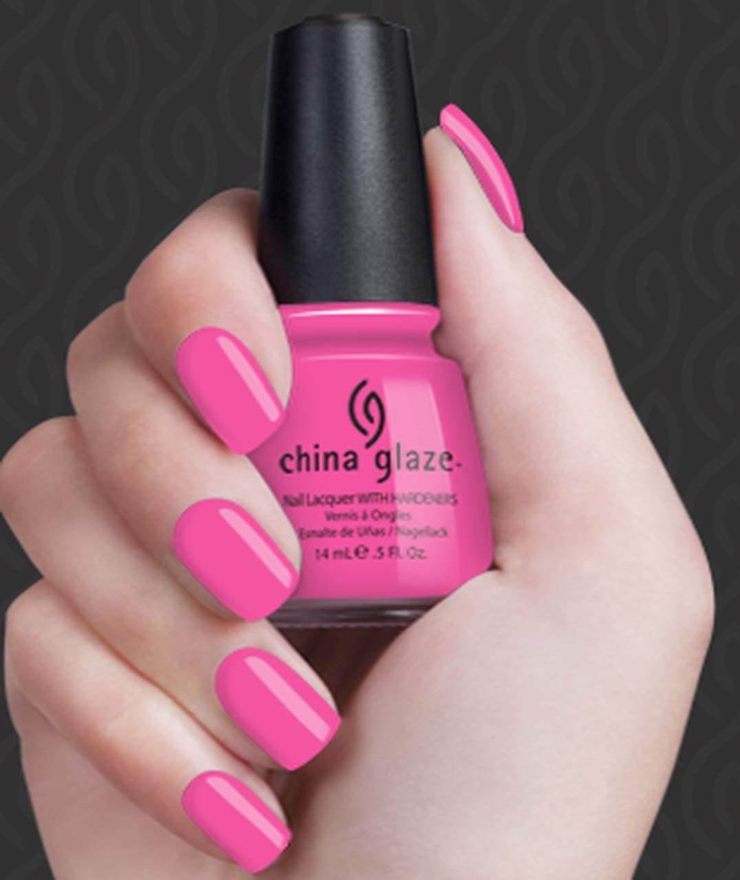 Hand with bubblegum pink nails holding the bottle on a dark patterned backdrop