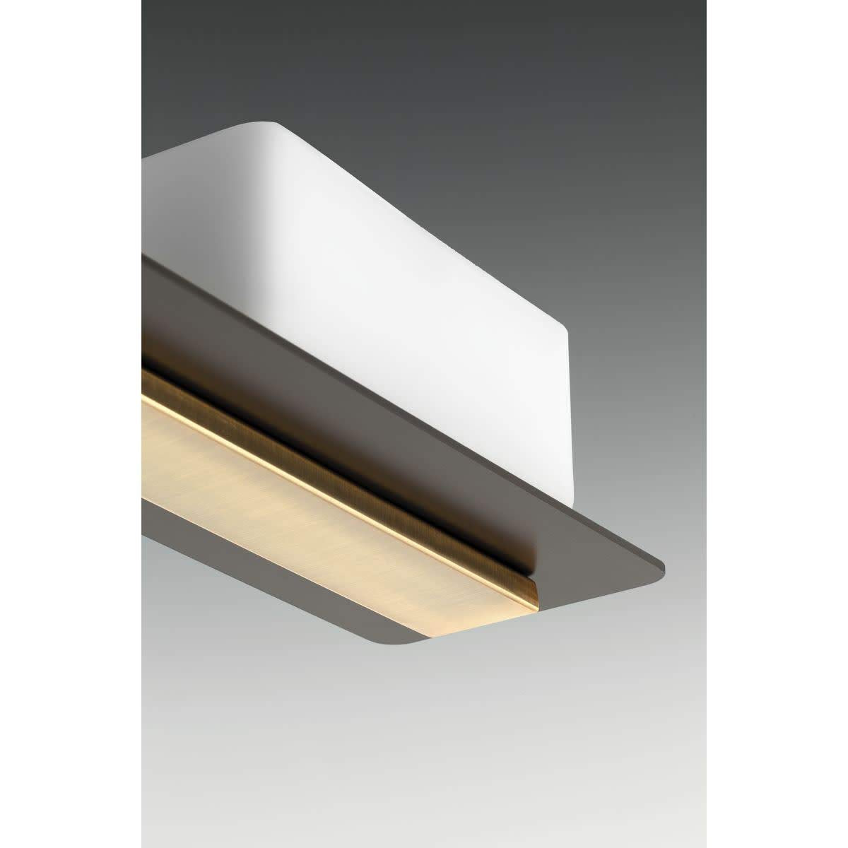 Underside close-up of a white glass shade over the dark bronze arm with a brass strip