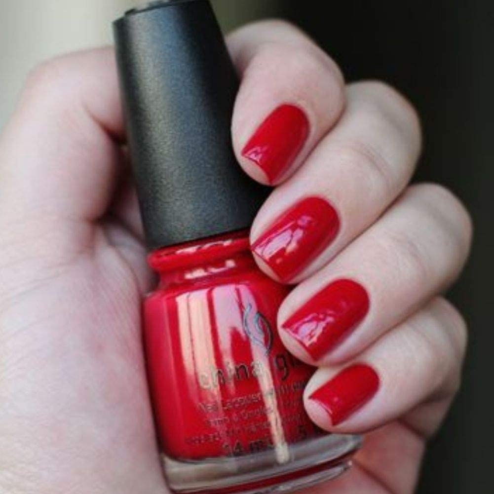 Hand with glossy red painted nails holding the red polish bottle