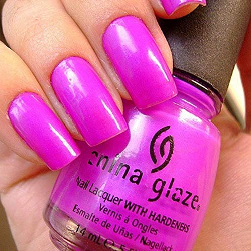 Close-up of long nails painted bright neon violet with the bottle behind