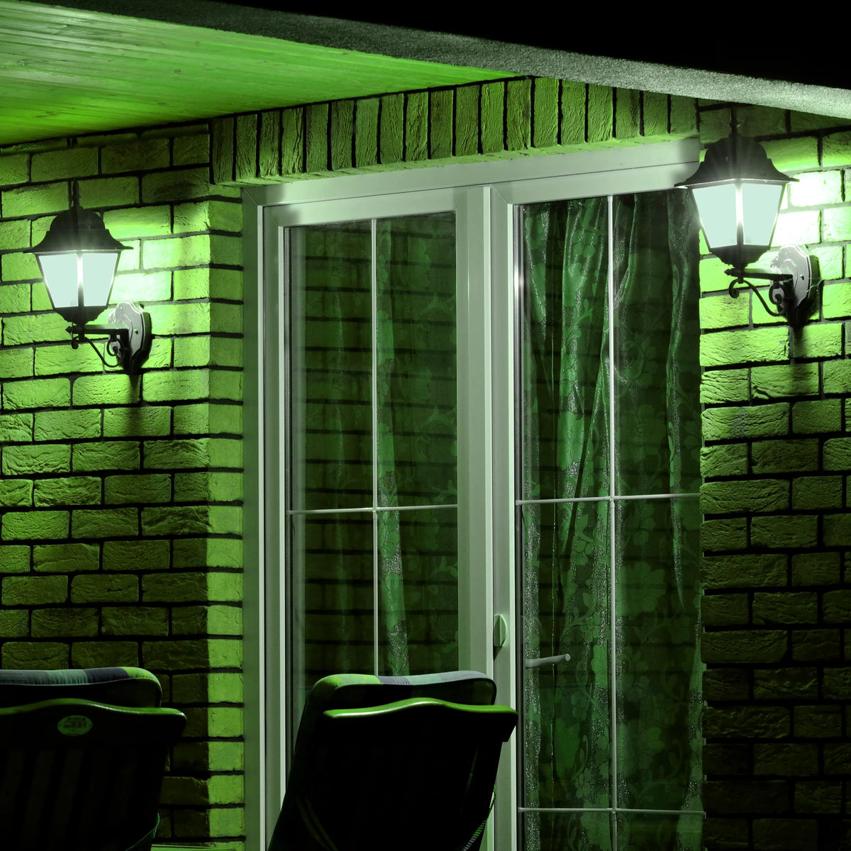 Two outdoor wall lanterns casting green light on a brick wall by patio doors