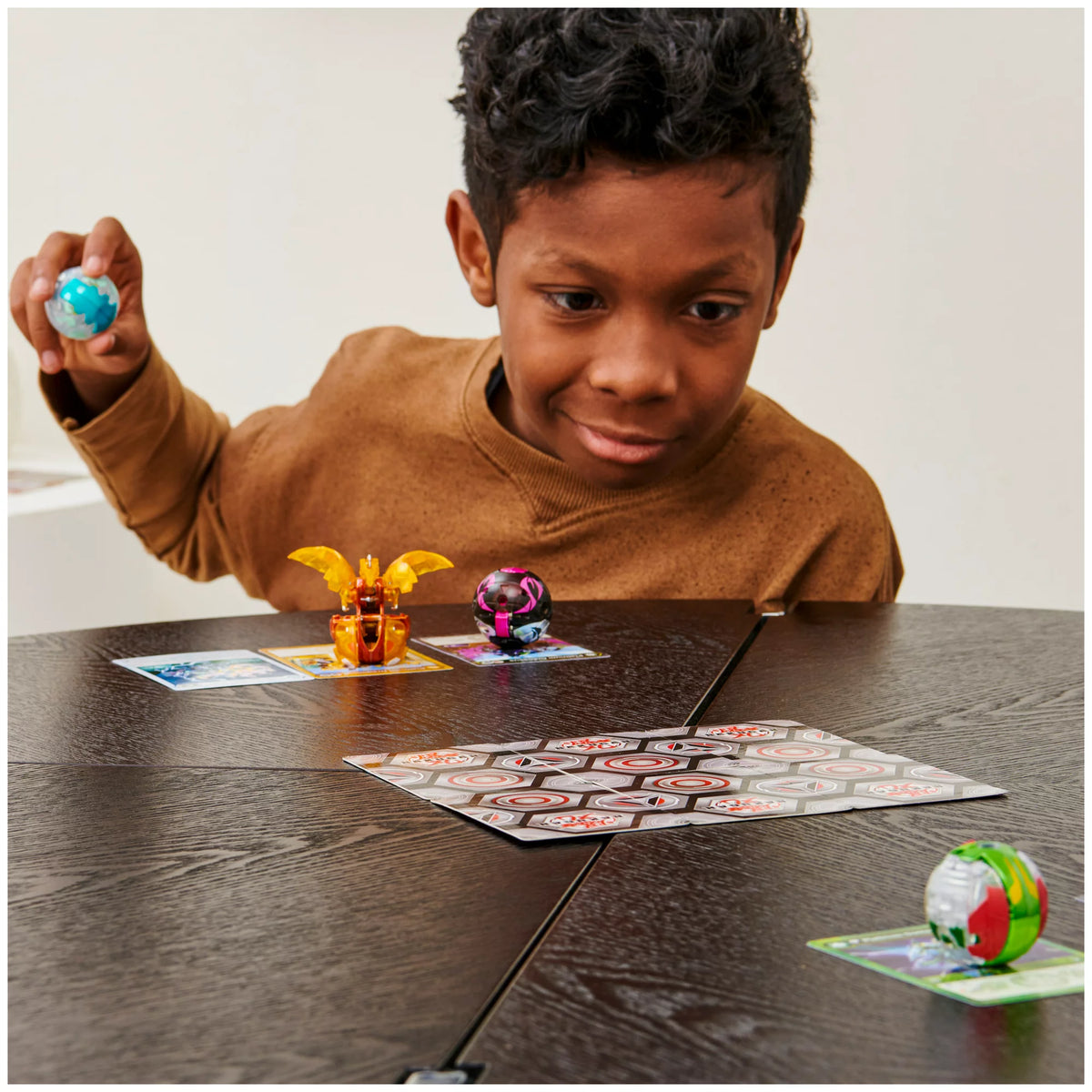 Boy holding a Bakugan ball with others arranged on a dark table