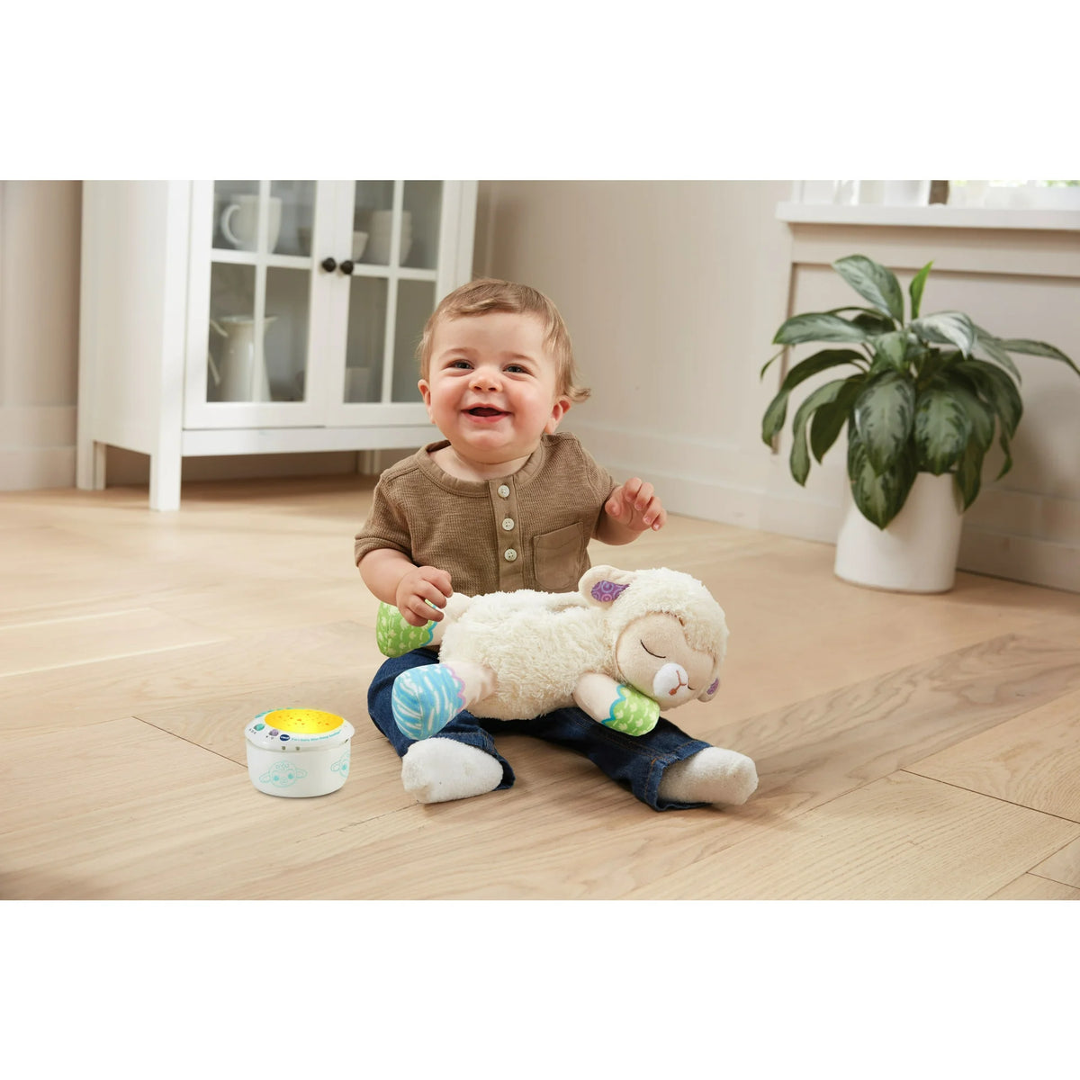 Smiling toddler on a wood floor with the plush lamb and glowing projector