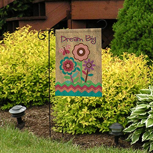 Dream Big burlap-print flag on a black stand in front of yellow shrubs