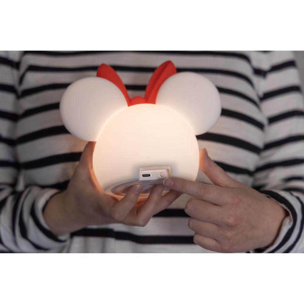 Hands holding the Minnie lamp glowing warm white, pointing to the USB-C port
