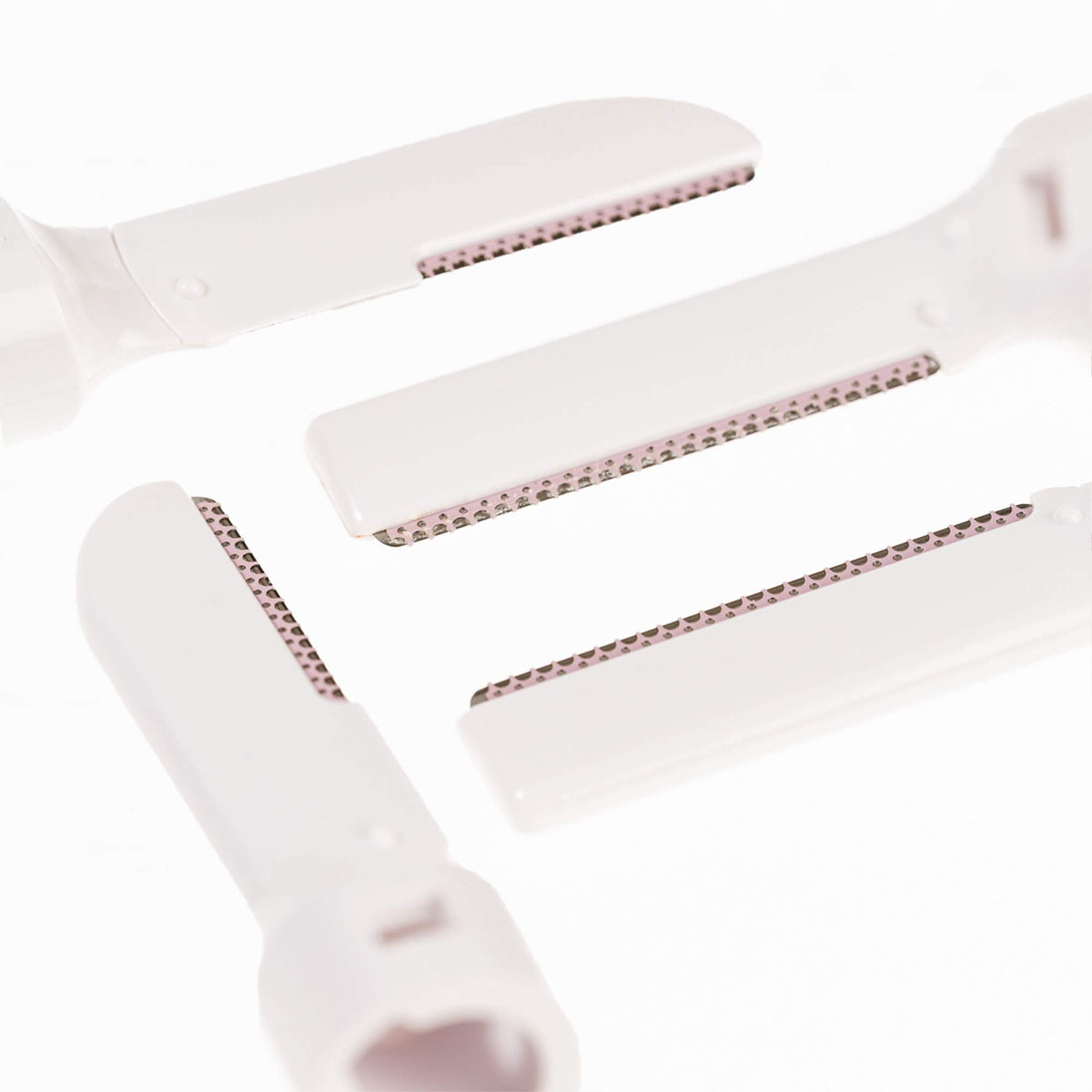 Four white facial and brow refill blades laid out showing their guarded edges