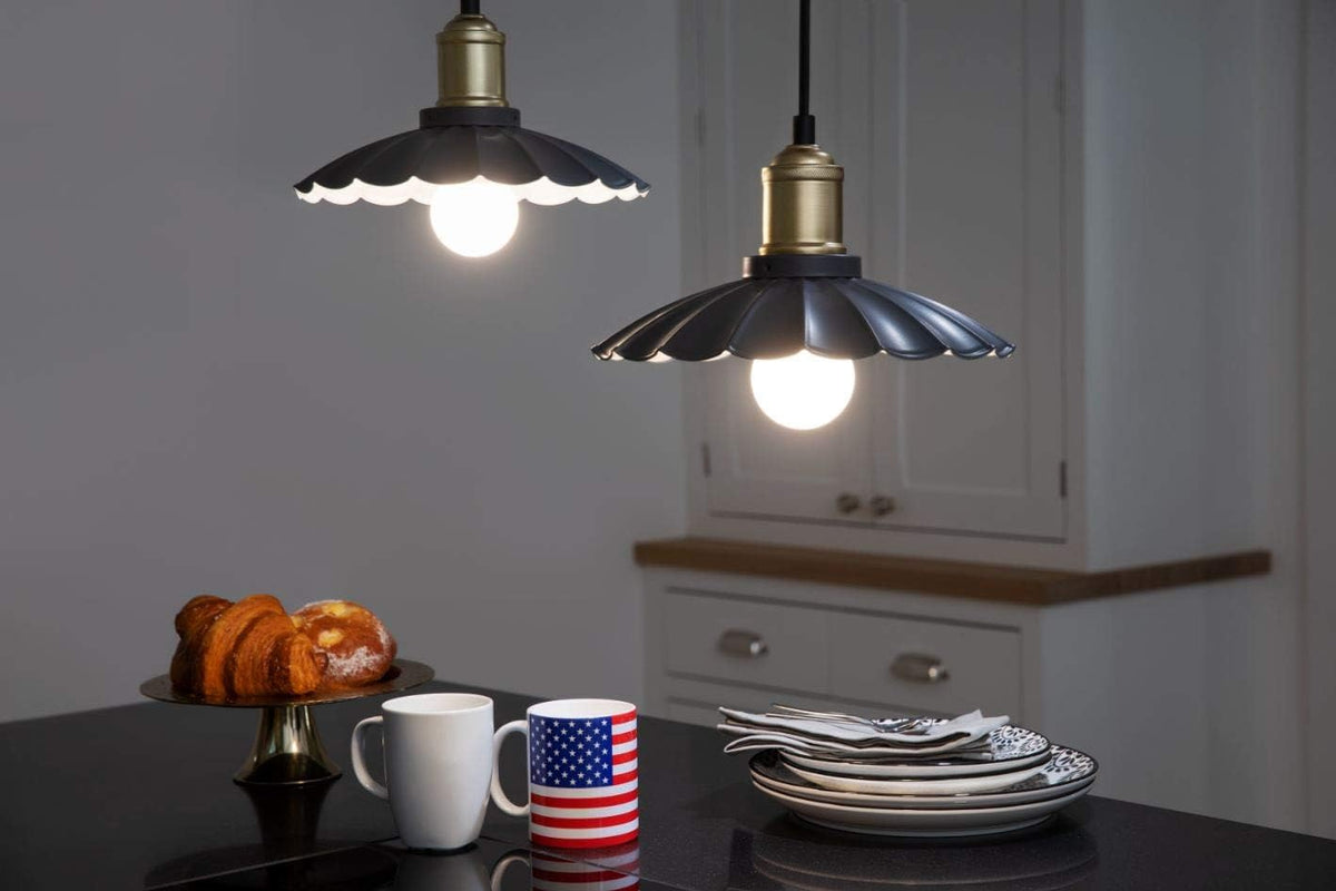 Two black scalloped pendant lamps with globe bulbs lit over a kitchen counter