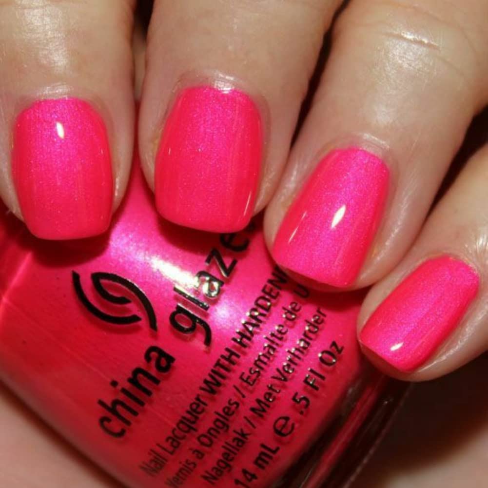 Close-up of nails painted shimmery neon pink beside the bottle