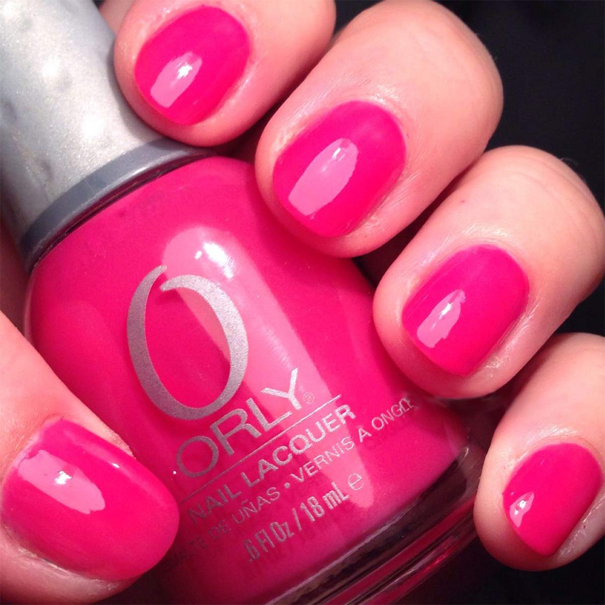 Hand with short nails painted bright pink holding an Orly polish bottle