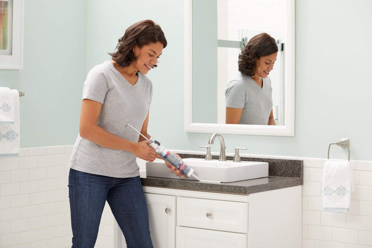 Woman sealing around a white bathroom basin with a caulk gun