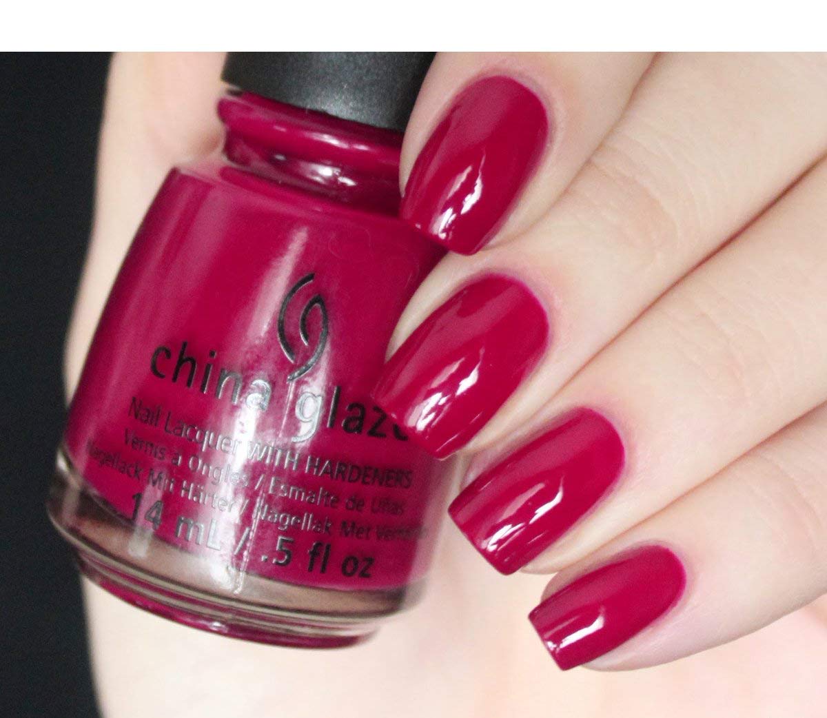 Nails painted raspberry red shown next to the matching bottle