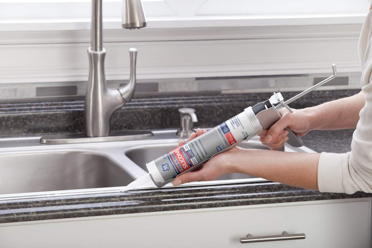 Hands sealing the edge of a stainless steel kitchen sink with a silicone cartridge