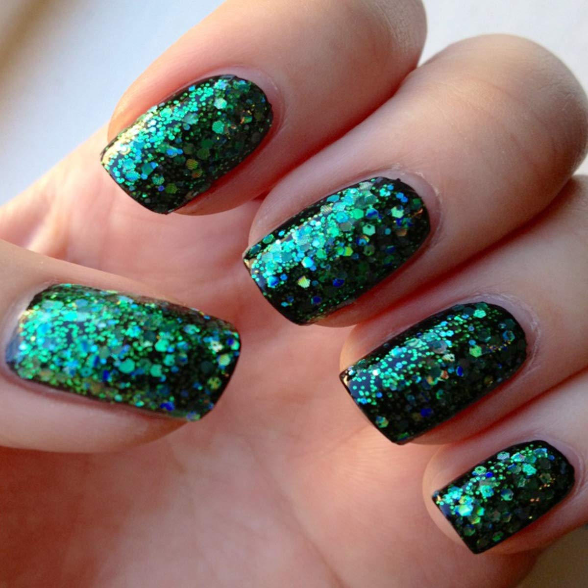 Nails painted with green holographic hexagon glitter over a dark base