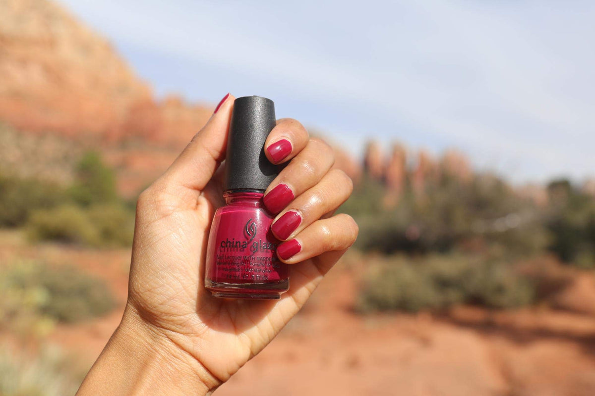 Hand with raspberry red nails holding the polish bottle outdoors