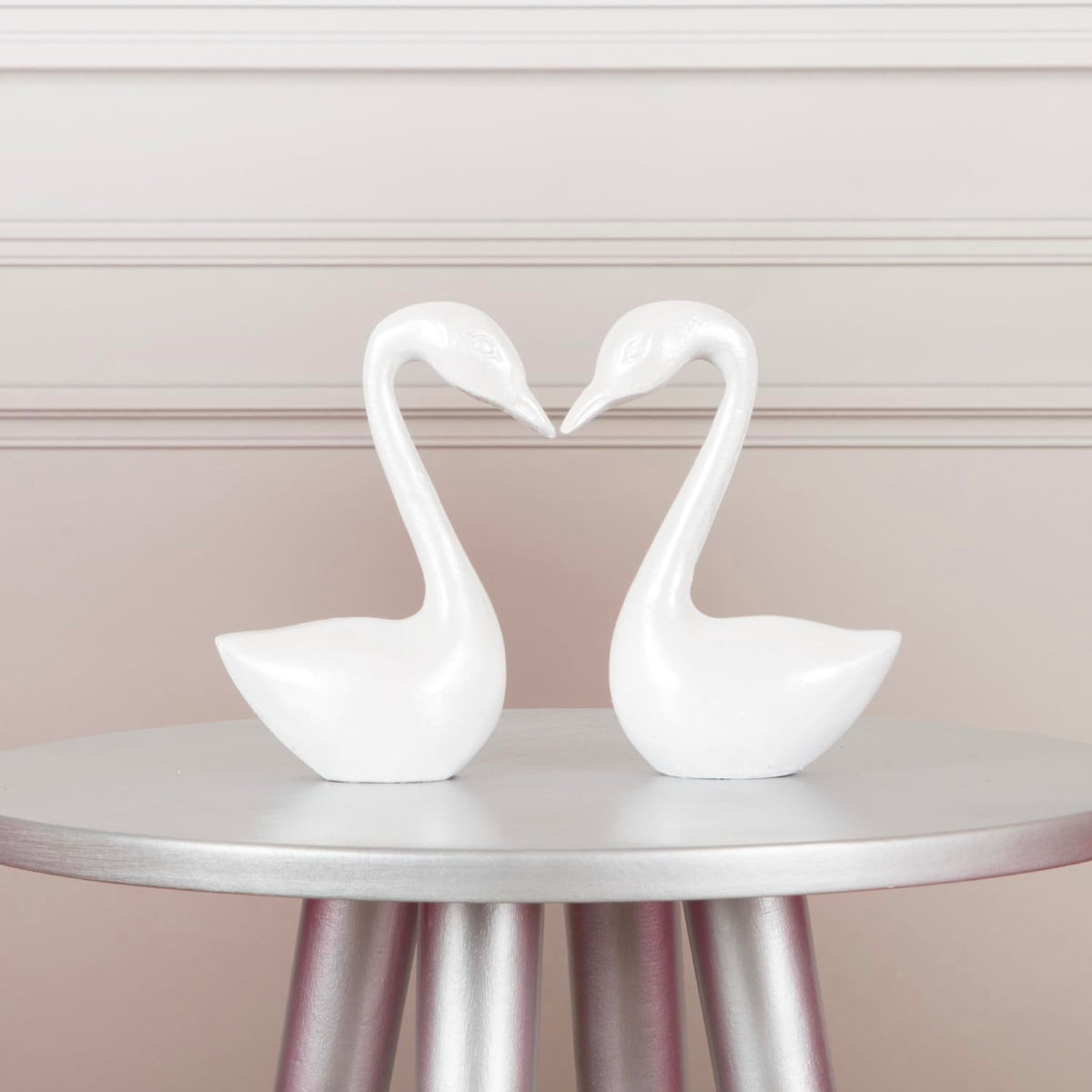 Pair of pearly white swan figurines forming a heart on a silver table