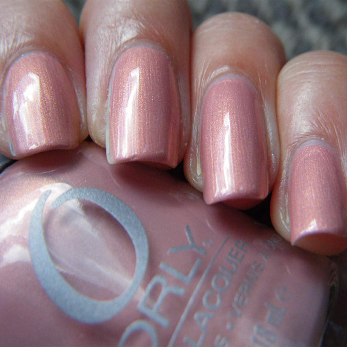 Close-up of nails painted in a dusty pink shimmer next to the Orly bottle