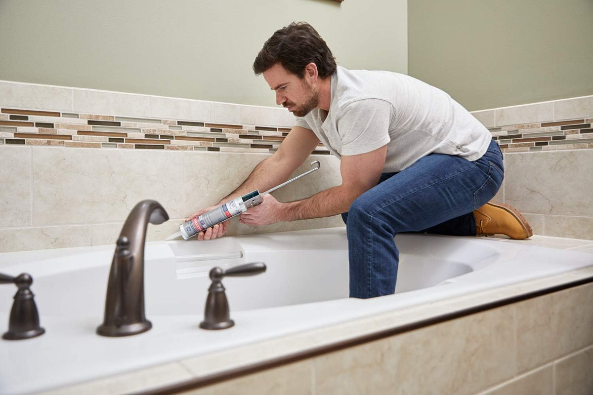 Man kneeling on a bathtub edge running silicone along the tile with a caulk gun