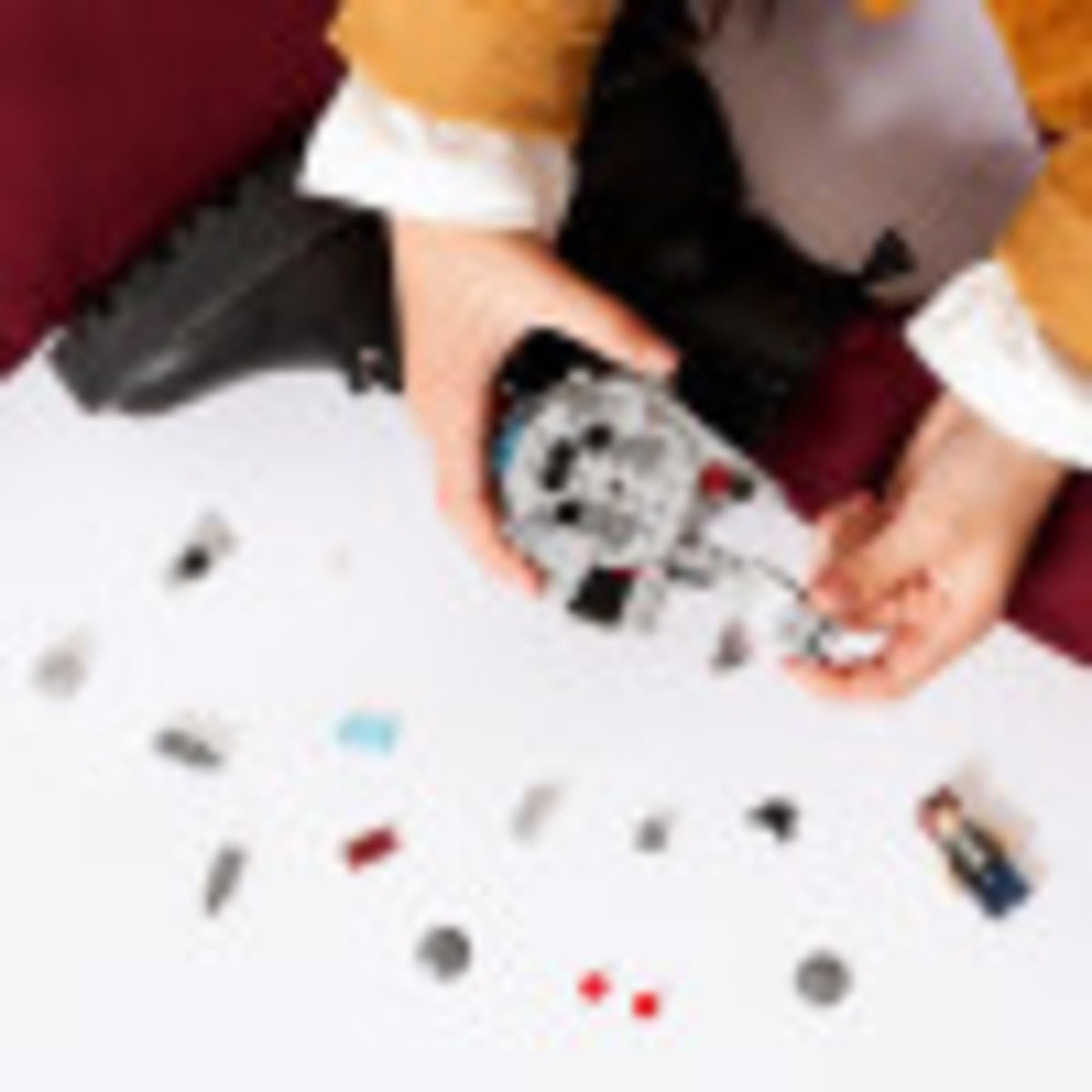Child's hands building the grey Falcon with loose bricks and a minifigure on the table