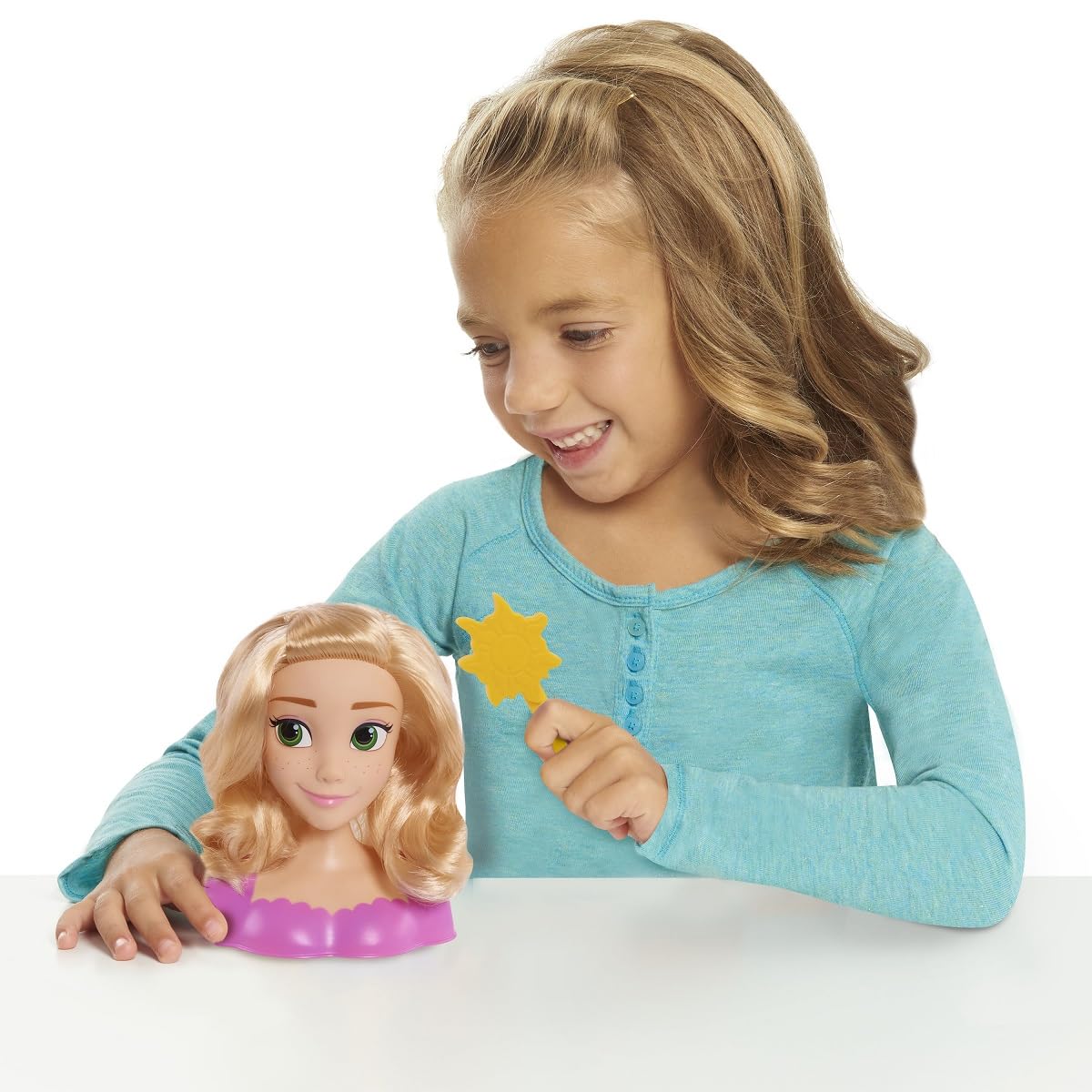 Smiling girl holding the sun brush beside the Rapunzel styling head on a table
