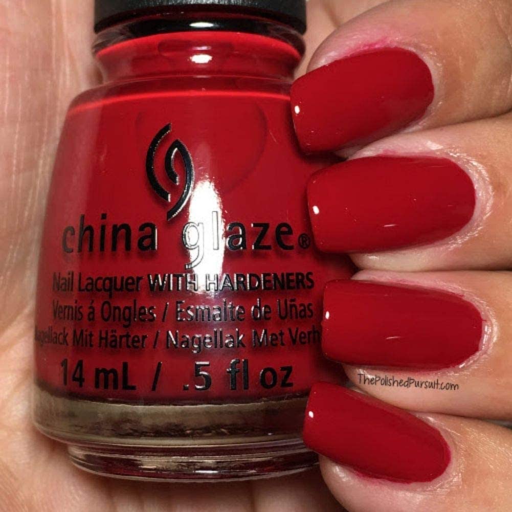 Hand with glossy deep red painted nails holding a red nail lacquer bottle