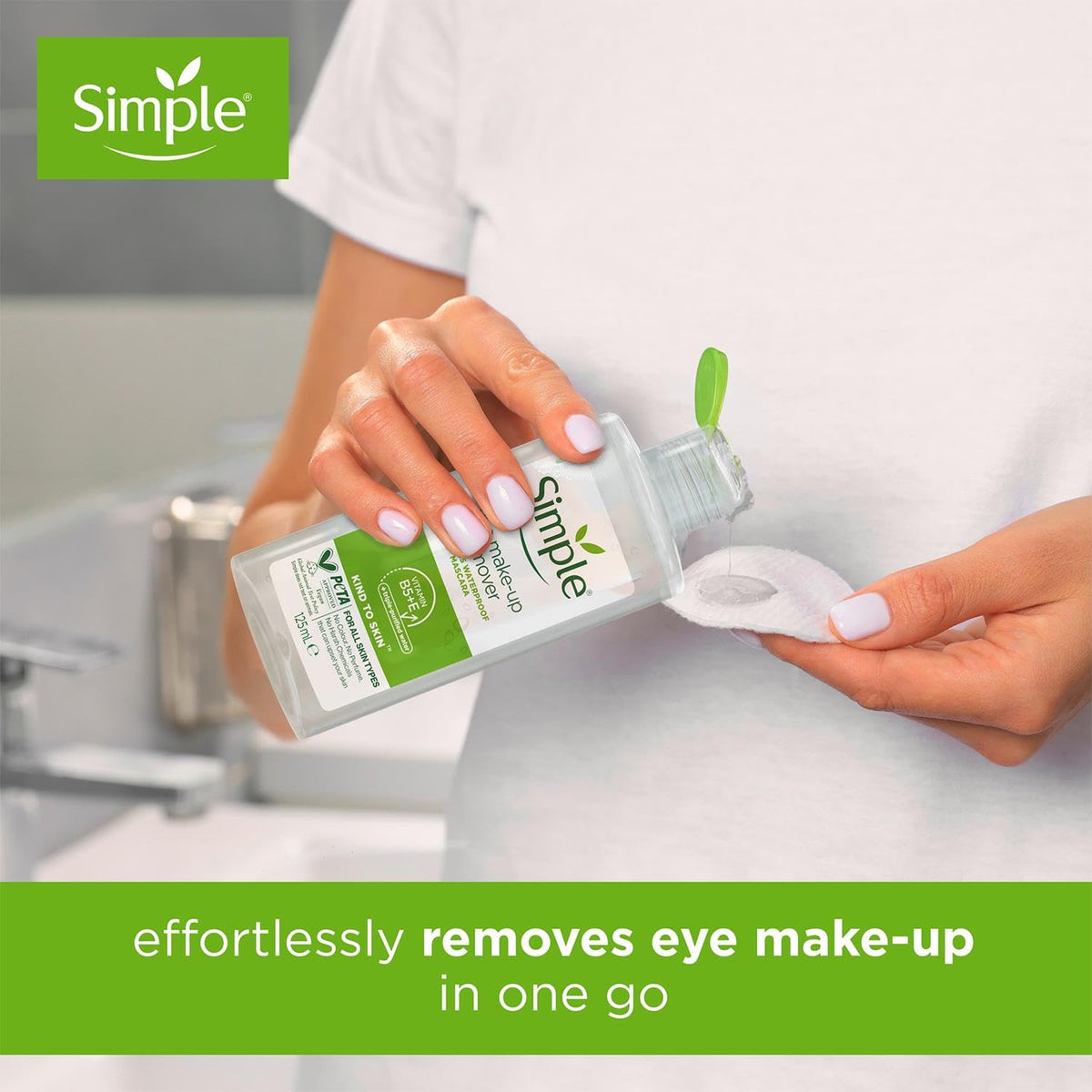 Hands pouring clear eye make-up remover onto a cotton pad at a bathroom sink